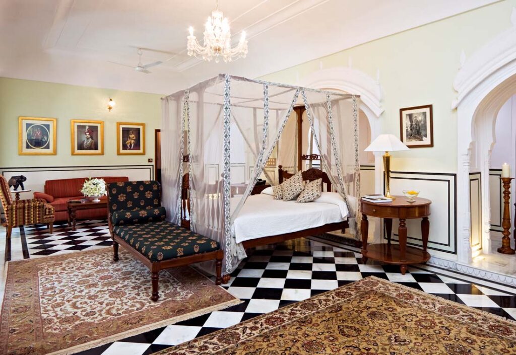 Where To Stay For a Soft Landing In India 15 Samode Haveli, room with a canopy bed, traditional rugs, and wall art of old historical figures